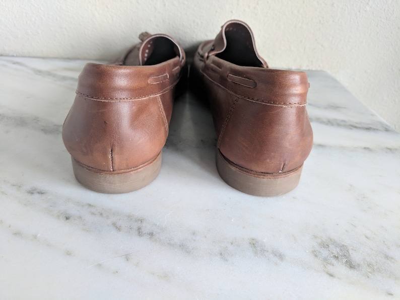 May include: A pair of brown leather loafers with a tassel detail. The loafers have a rubber sole and are shown from the back.
