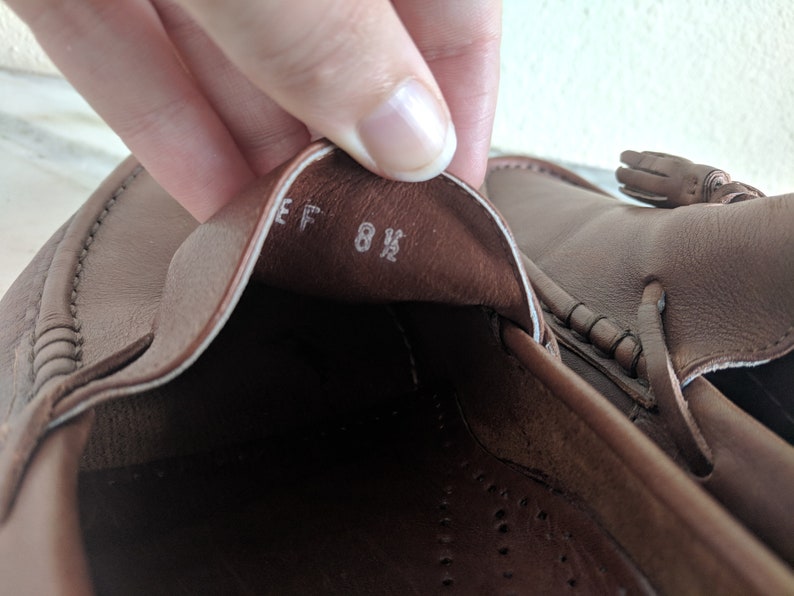 May include: Close-up of the inside of a brown leather loafer with a white label that reads "EF 8 1/2".