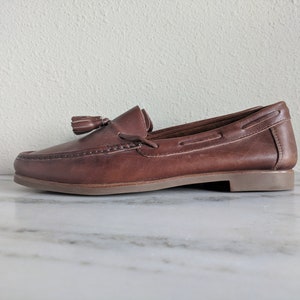 May include: Brown leather tassel loafers with a brown leather sole.