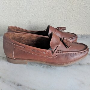 May include: A pair of brown leather tassel loafers. The loafers have a simple design and are made of a high-quality leather.