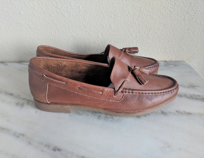 May include: A pair of brown leather tassel loafers. The loafers have a simple design and are made of a high-quality leather.