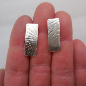 May include: A pair of silver earrings with a textured, sunburst design.