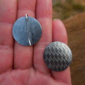 May include: Two round metal pendants with different patterns. One pendant has a wavy pattern and the other has a checkered pattern.