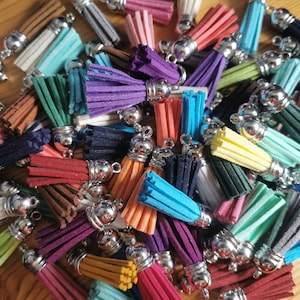 May include: A collection of colourful tassel charms with silver metal rings. The tassels are made of soft, fuzzy material and come in a variety of colours, including pink, blue, green, red, purple, and yellow.