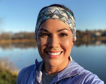 May include: A woman wearing a blue jacket with the Patagonia logo, a patterned headband, and a white shirt. She is smiling and standing in front of a lake.