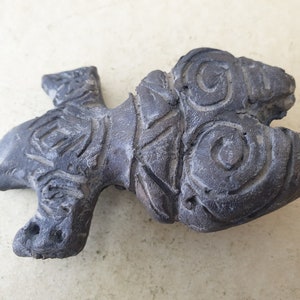 May include: A dark gray ceramic sculpture of a stylized fish with intricate swirling patterns and geometric designs.