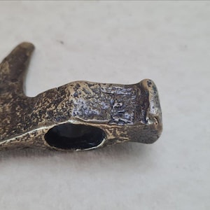 May include: A small, antique-looking bronze axe head with a rounded edge and a hole in the center. The axe head has a worn, aged appearance.