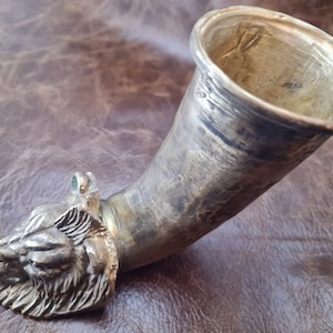 May include: A silver metal drinking horn with a detailed animal head at the base. The horn is slightly tarnished and has a smooth, polished interior.