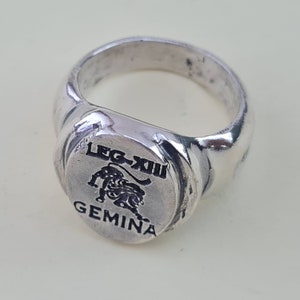 K&ouml;nnte beinhalten: Ein silberner Ring mit einem schwarzen L&ouml;wenmotiv und dem Text "LEG-XIII GEMINA".