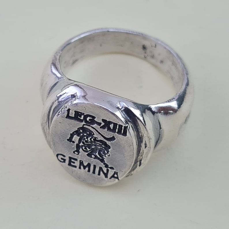 K&ouml;nnte beinhalten: Ein silberner Ring mit einem schwarzen L&ouml;wenmotiv und dem Text "LEG-XIII GEMINA".