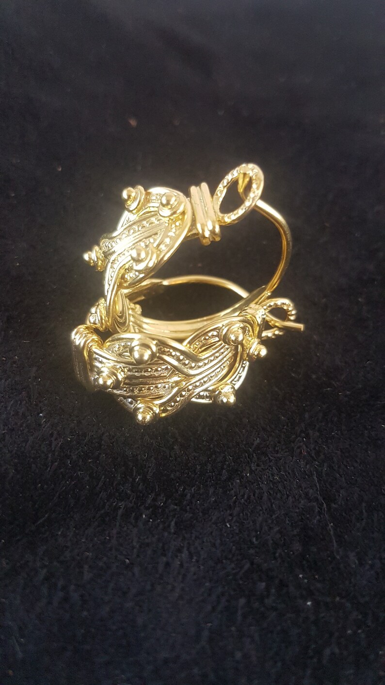 Op de afbeelding: Gouden creolen met een gedetailleerd, ingewikkeld ontwerp. De oorbellen zijn gemaakt van een geweven patroon met kleine kralen en een ronde accent.