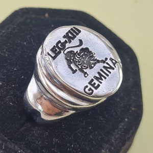 K&ouml;nnte beinhalten: Silberring mit einer ovalen Oberseite, die einen L&ouml;wen und den Text "LEG XII GEMINA" zeigt.
