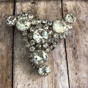 May include: A silver tone brooch with a cluster of clear rhinestones in a triangular shape.