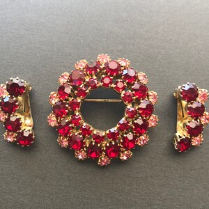 May include: A set of three vintage jewellery pieces featuring a large red and pink rhinestone brooch in the shape of a wreath, and two smaller matching earrings.
