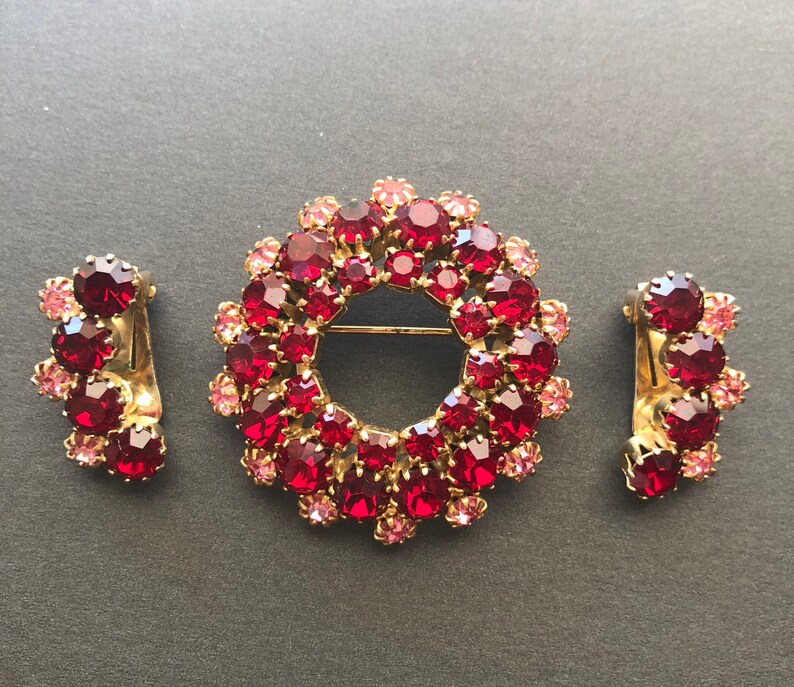 May include: A set of three vintage jewellery pieces featuring a large red and pink rhinestone brooch in the shape of a wreath, and two smaller matching earrings.