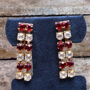 Op de afbeelding: Een paar oorhangers met afwisselend rode en witte vierkante strass steentjes. De oorhangers zijn goudkleurig en hebben een eenvoudig ontwerp.