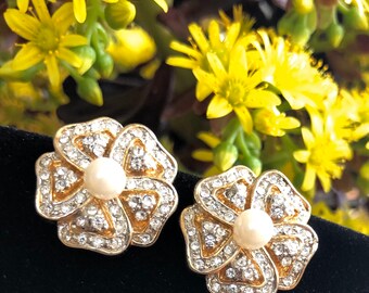 May include: A pair of gold tone flower-shaped earrings with clear rhinestones and a pearl center.