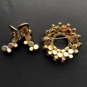 May include: A gold-tone brooch and a pair of earrings with a circular design of small, round, clear rhinestones.