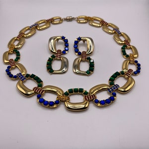 May include: A gold-tone necklace and earrings set with a chain link design. The links are decorated with blue, green, and red rhinestones.
