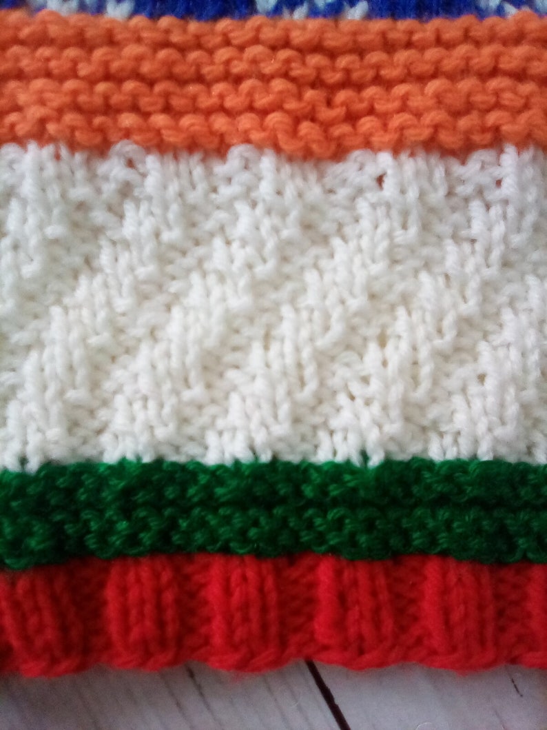 Peut inclure: Un tissu tricot&eacute; avec des rayures orange, blanches, vertes et rouges. Le tissu est r&eacute;alis&eacute; avec une vari&eacute;t&eacute; de points, cr&eacute;ant un aspect textur&eacute;.