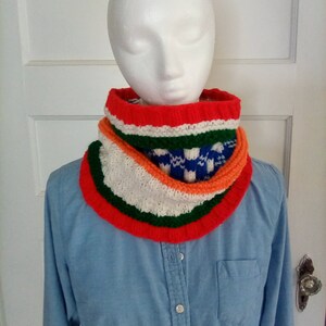 Peut inclure: Un chauffe-cou color&eacute; en tricot avec des rayures rouges, orange, vertes, blanches et bleues. Le chauffe-cou est port&eacute; par un mannequin.