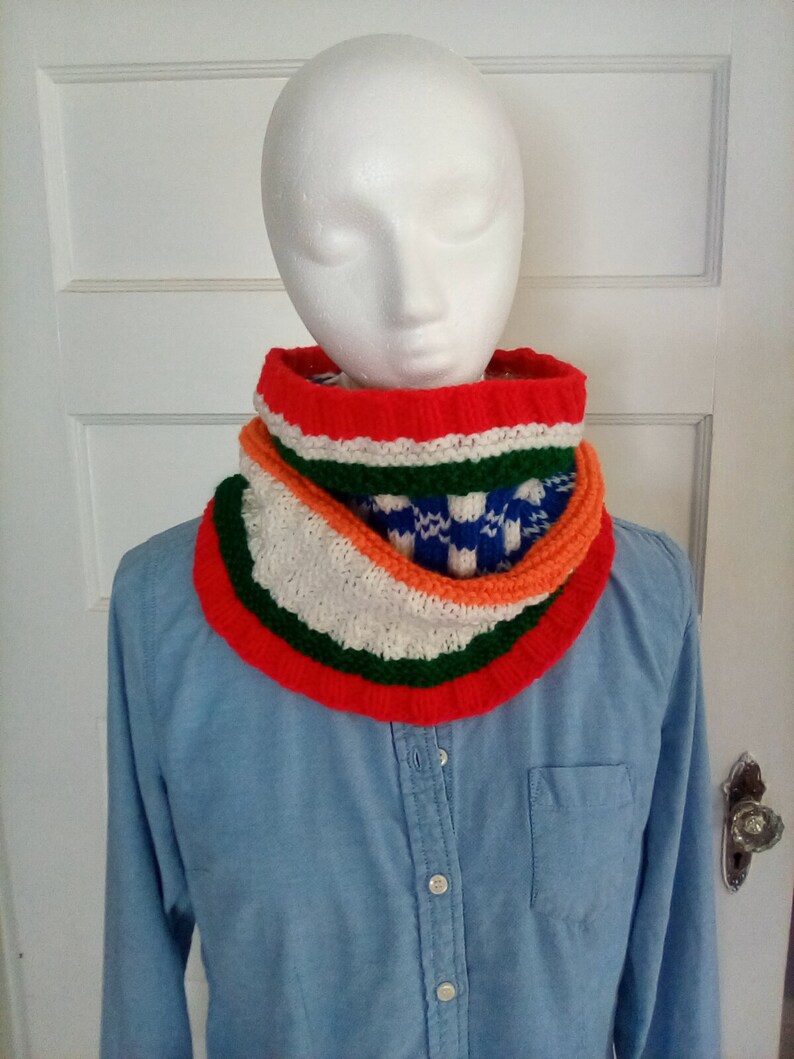 Peut inclure: Un chauffe-cou color&eacute; en tricot avec des rayures rouges, orange, vertes, blanches et bleues. Le chauffe-cou est port&eacute; par un mannequin.