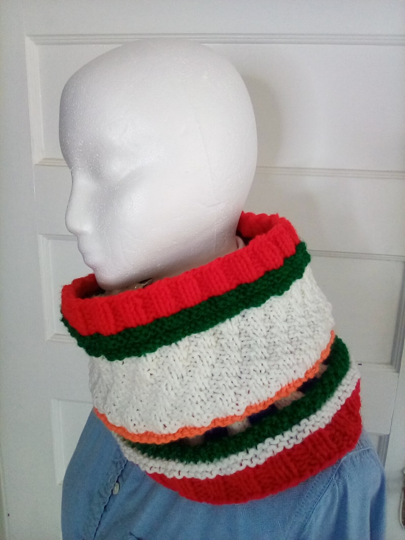 Peut inclure: Un tour de cou en tricot ray&eacute; blanc, rouge, vert et orange. Le tour de cou est fait de fil doux et est parfait pour se tenir au chaud en hiver.