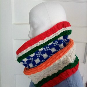 Peut inclure: Un chauffe-cou color&eacute; en tricot avec des rayures rouges, blanches, vertes, orange et bleues. Le chauffe-cou a un motif &agrave; carreaux au milieu.