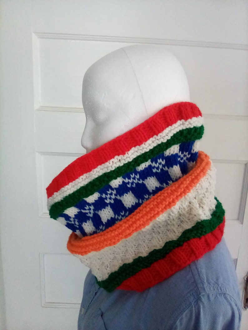 Peut inclure: Un chauffe-cou color&eacute; en tricot avec des rayures rouges, blanches, vertes, orange et bleues. Le chauffe-cou a un motif &agrave; carreaux au milieu.