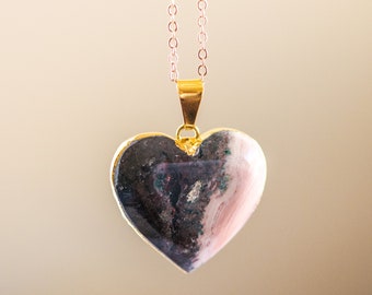 May include: A gold heart-shaped pendant necklace with a pink and black marbled resin inlay.