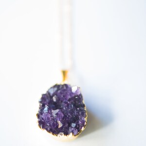 May include: A gold chain necklace with a purple amethyst crystal pendant. The crystal is a cluster of small, faceted stones.