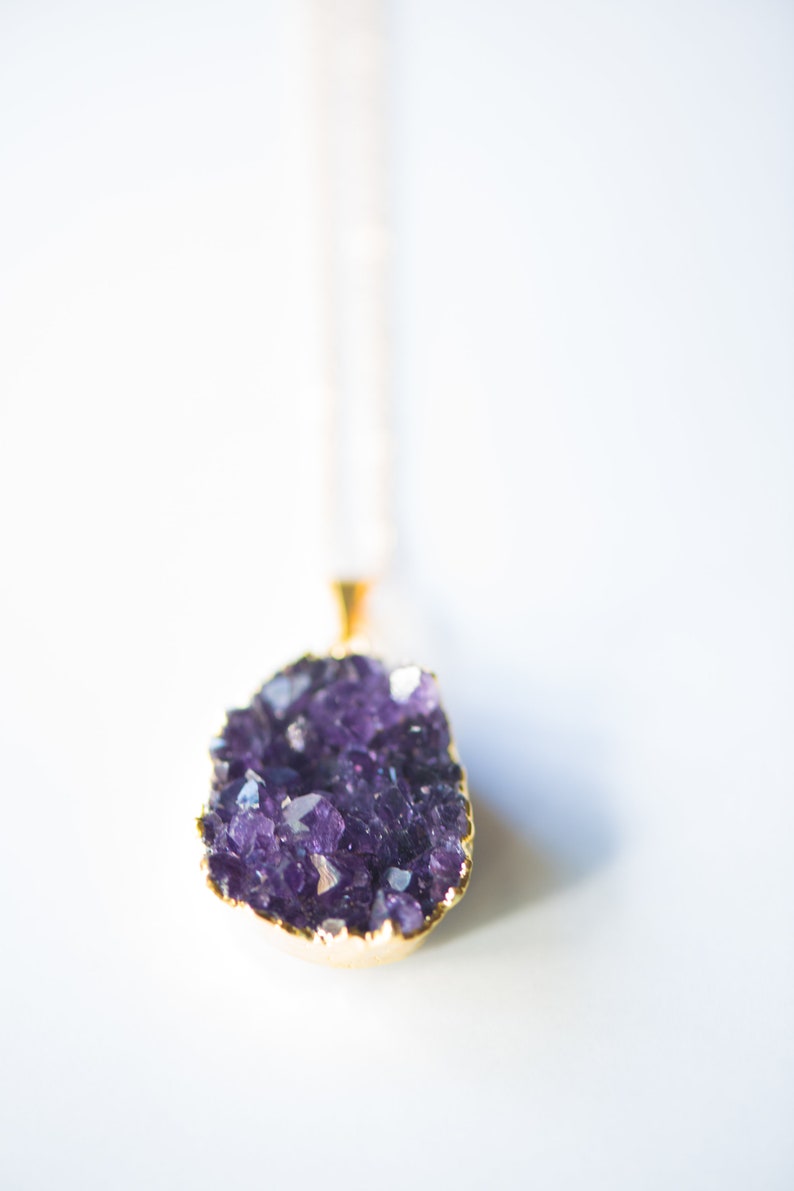 May include: A gold chain necklace with a purple amethyst crystal pendant. The crystal is a cluster of small, faceted stones.