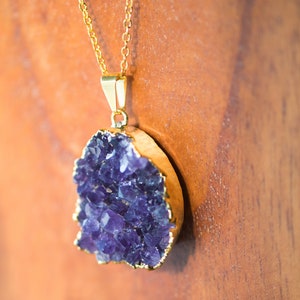 May include: A gold chain necklace with a large amethyst pendant. The amethyst is a cluster of purple crystals.
