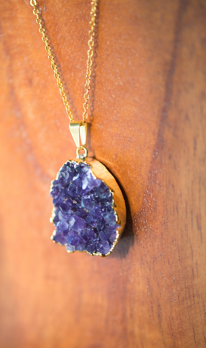 May include: A gold chain necklace with a large amethyst pendant. The amethyst is a cluster of purple crystals.