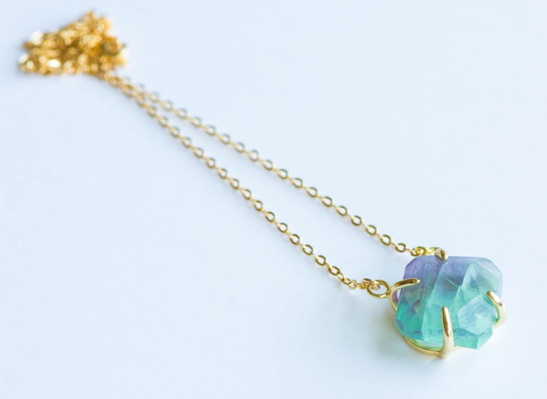 May include: A gold chain necklace with a large, faceted, green and purple fluorite pendant.