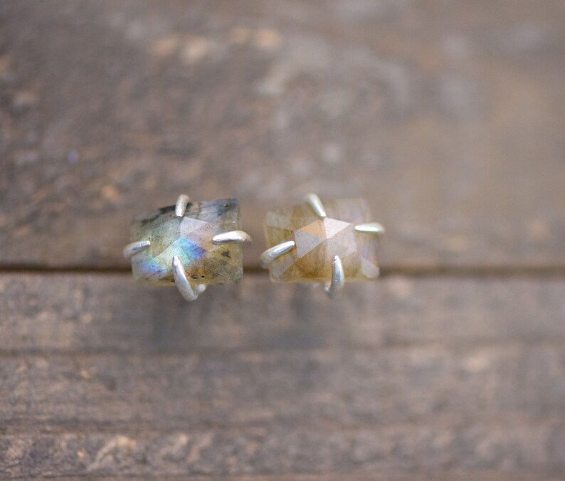 Pu&ograve; includere: Un paio di orecchini d'argento con pietre preziose di labradorite iridescente. Le pietre preziose sono di forma quadrata e hanno un taglio sfaccettato.