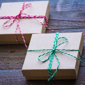 Peut inclure: Deux bo&icirc;tes cadeaux envelopp&eacute;es de papier brun avec de la ficelle. La bo&icirc;te de gauche est attach&eacute;e avec de la ficelle rouge et blanche. La bo&icirc;te de droite est attach&eacute;e avec de la ficelle verte et blanche.