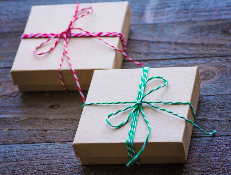 Peut inclure: Deux bo&icirc;tes cadeaux envelopp&eacute;es de papier brun avec de la ficelle. La bo&icirc;te de gauche est attach&eacute;e avec de la ficelle rouge et blanche. La bo&icirc;te de droite est attach&eacute;e avec de la ficelle verte et blanche.