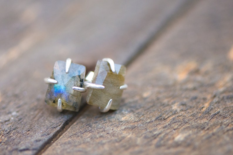 Pu&ograve; includere: Un paio di orecchini d'argento con pietre di labradorite iridescenti incastonate in un design geometrico semplice.