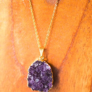 May include: A gold chain necklace with a large, purple amethyst pendant. The pendant is a cluster of crystals with a natural, irregular shape.