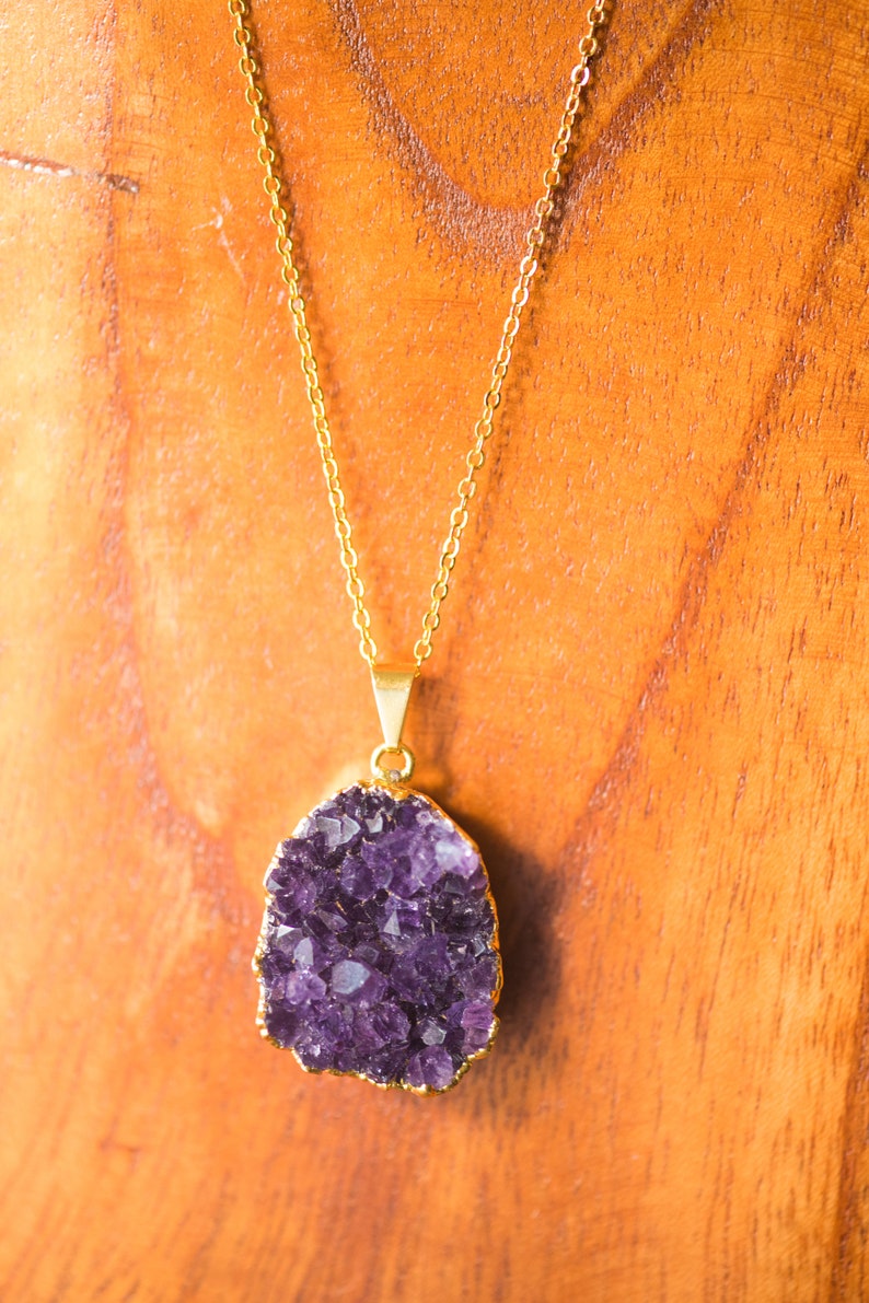 May include: A gold chain necklace with a large, purple amethyst pendant. The pendant is a cluster of crystals with a natural, irregular shape.