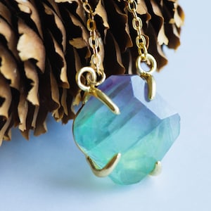 May include: A gold chain necklace with a large, faceted, green and purple fluorite pendant.