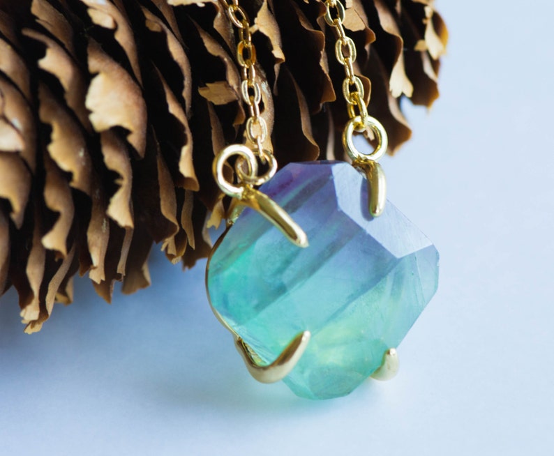 May include: A gold chain necklace with a large, faceted, green and purple fluorite pendant.