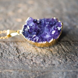 May include: A gold chain necklace with a large amethyst crystal pendant. The crystal is a cluster of purple crystals with a gold-plated edge.