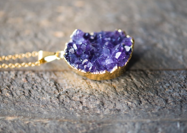 May include: A gold chain necklace with a large amethyst crystal pendant. The crystal is a cluster of purple crystals with a gold-plated edge.