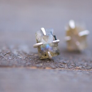 Pu&ograve; includere: Un paio di orecchini d'argento con pietre di labradorite iridescenti incastonate in una montatura a quattro griffe.
