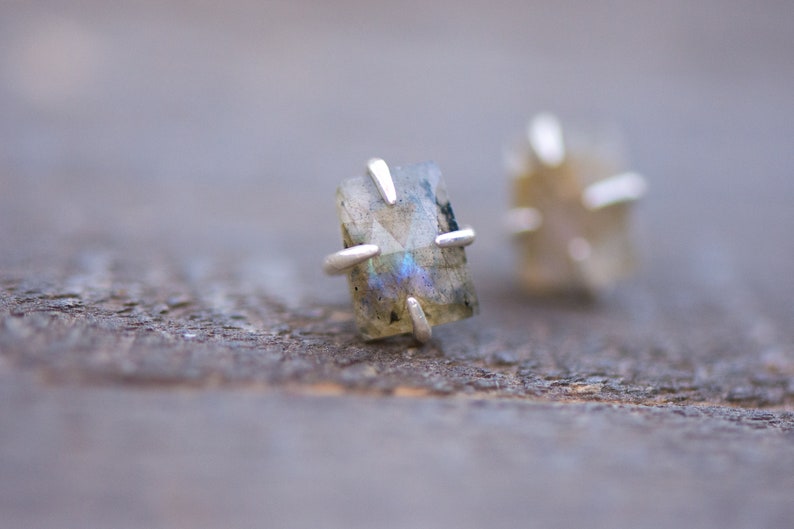 Pu&ograve; includere: Un paio di orecchini d'argento con pietre di labradorite iridescenti incastonate in una montatura a quattro griffe.