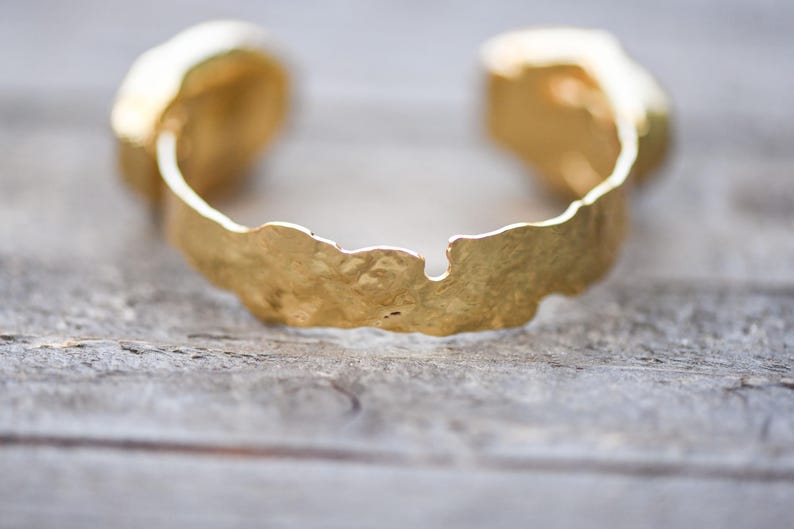 May include: A gold-toned bracelet with a textured, irregular design. The bracelet is open and has a slightly curved shape.