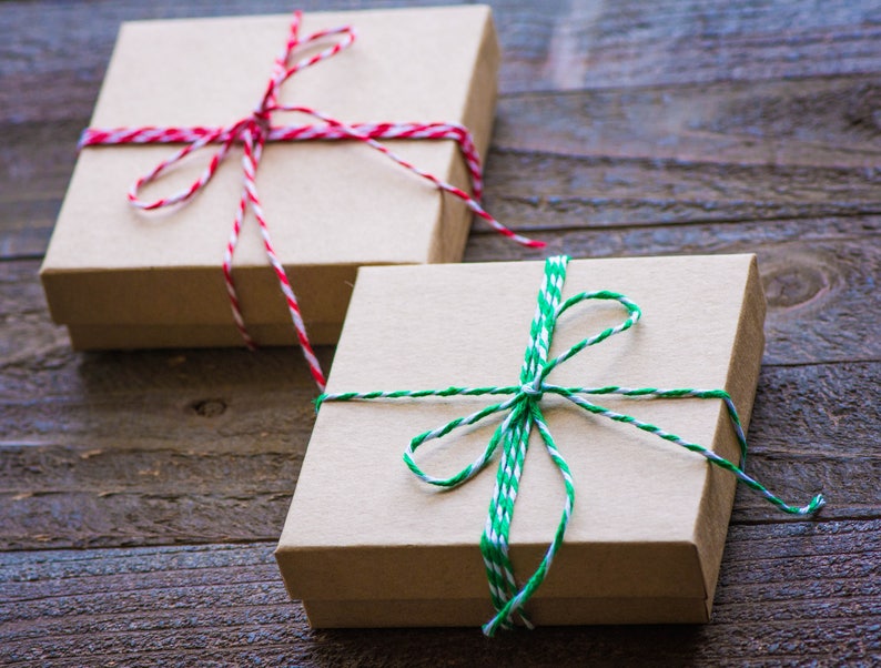 Pu&ograve; includere: Due scatole regalo avvolte in carta marrone con spago. Una scatola &egrave; legata con spago rosso e bianco, l'altra con spago verde e bianco.