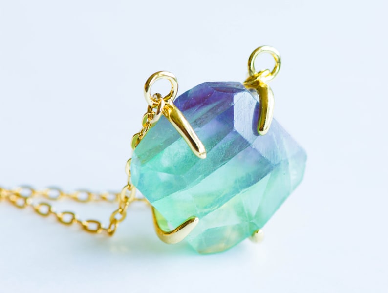 May include: A gold necklace with a large, faceted fluorite pendant. The fluorite is a vibrant green and blue color.